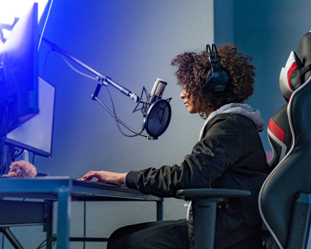 Professional Girl Gamer Plays in Video Game on Her Computer. She’s Participating in Online Cyber Games Tournament, Plays at Home, or in Internet Cafe. She Wears Gaming Headset. jugadora de gaming en su ordenador